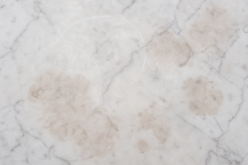 Close-up view of a marble countertop with visible etching and staining caused by acidic spills.